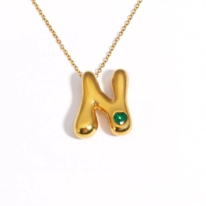 Detail of 18k gold plated puffy bubble letter N pendant with a green heart gemstone