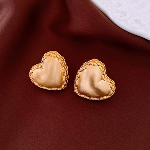 Détail de boucles d'oreilles cœur doré avec fini brossé mat et bords à texture tissée