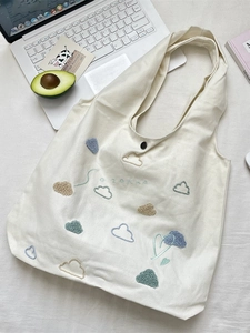 Off-white canvas tote bag with colorful embroidered clouds and hearts on a flat surface