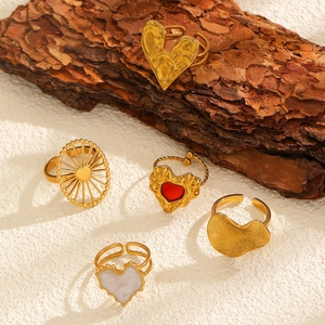 Detail of adjustable gold heart rings with enamel and shell on natural bark background