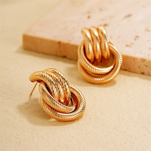 Macro close-up of gold-plated twisted rope knot stud earrings on a beige stone