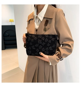 Detail of black floral embossed clutch bag held by model wearing a khaki trench coat