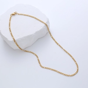 Macro detail of golden Figaro chain necklace resting on a white textured stone surface