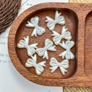 Detail shot of pearlescent white resin butterfly beads in a natural wooden tray for DIY crafts