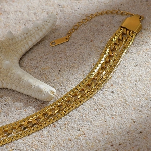 Detail of layered gold-plated stainless steel bracelets on sand with a white starfish