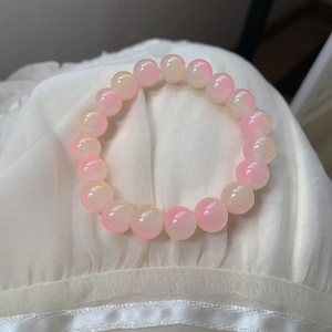 Detail of pink and yellow gradient crystal beaded bracelet on white silk fabric background