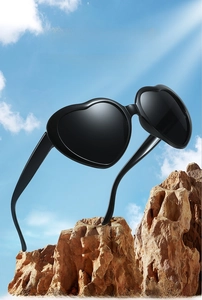 Detailed view of black heart-shaped oversized sunglasses set against a bright blue sky