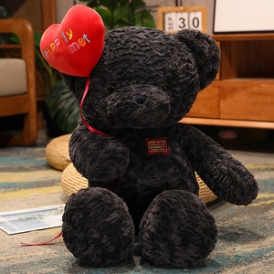 Detail of a black plush teddy bear holding a red heart with happily met text