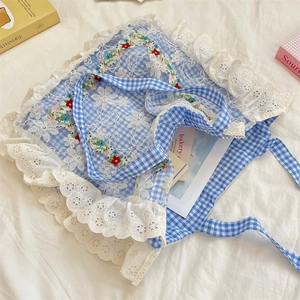 Detail of floral embroidery and white lace trim on a blue gingham canvas tote bag