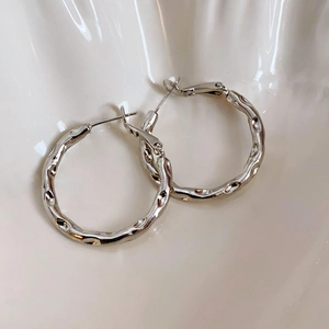 Close-up of silver geometric hoop earrings with hammer texture on white ceramic tray
