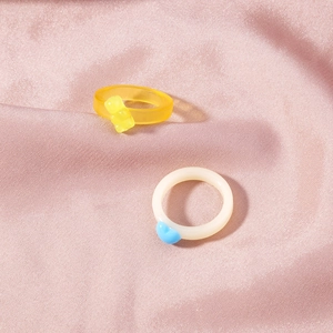 Detail of yellow crystal bear ring and milky white heart ring on pink silk fabric