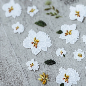 3D floral nail stickers with white embossed flowers and dark green leaves on grey fabric