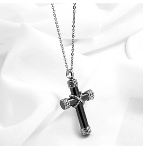 Detail view of a black stainless steel cross urn necklace on white fabric background