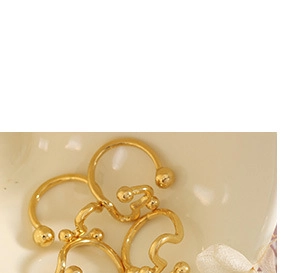 Detailed view of stacked gold ear cuffs with round ball ends on a white surface