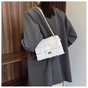 Detail of white denim crossbody bag with frayed edges and gold chain strap on shoulder