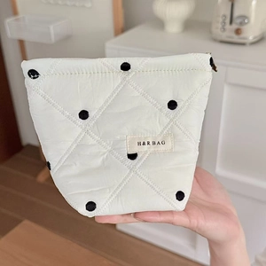 Gros plan d'une trousse à maquillage blanche matelassée à pois noirs avec logo de marque