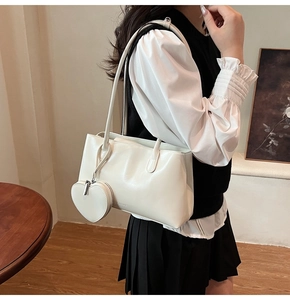 Détail du sac à bandoulière crème en cuir mat avec charm de cœur porté par un mannequin