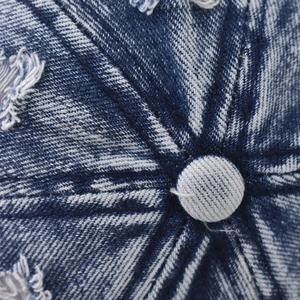 Close-up of distressed denim baseball cap top button with vintage stitching details
