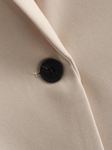 Close-up of beige twill fabric and a premium black four-eye button on a loose blazer