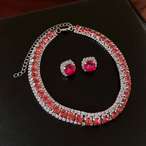 Flat lay view of a red gemstone necklace and stud earrings set on black leather texture