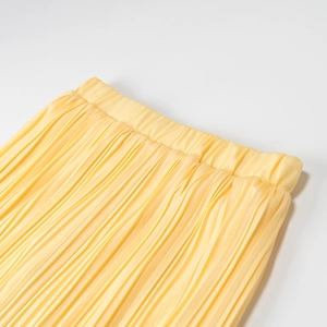 Détail de la taille d'une jupe plissée jaune montrant la texture et la qualité
