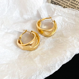 Macro detail of gold double-layered hoop earrings on a textured paper background