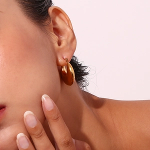 Polished 18K gold plated thick oval hoop earring worn by a model in soft lighting