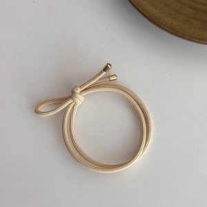 Détail d'un élastique à cheveux beige avec un fermoir métallique doré de style minimaliste