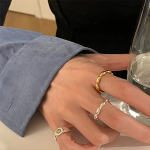 Primer plano de anillos retorcidos de oro y plata con un anillo de sello smiley en la mano