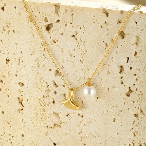 Macro detail of gold ginkgo leaf and pearl pendant on a thin necklace over stone