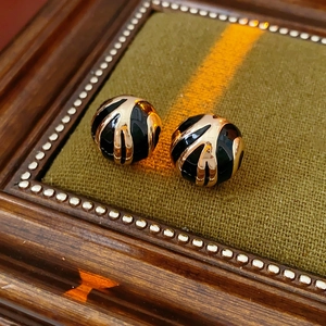 Close-up of black and gold enamel ball earrings with elegant striped texture design