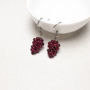 Detail showing handmade deep red garnet grape cluster earrings on a white ceramic bowl