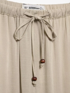 Detail of khaki wide-leg trousers showing elastic waist with drawstring and wooden beads