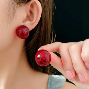 Translucent red resin round stud earrings with gold foil flakes on model's ear