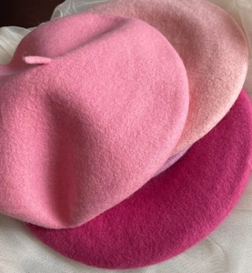 Close-up of three layered wool beret hats in gradient pink tones with thick felt texture