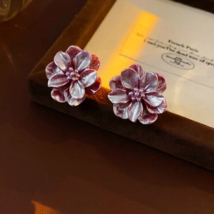 Vue macro de boucles d'oreilles fleurs en résine violet foncé sur un présentoir velours