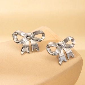 Detail view of silver bow-shaped stainless steel earrings on a beige stone display base