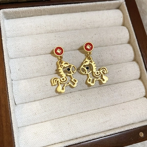 Détail de boucles d'oreilles cheval dorées avec clous rouges sur velours beige