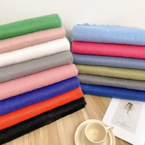 Thick mohair scarves in multiple colors with tassels shown neatly folded on a wooden table