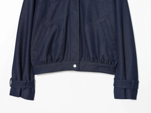 Detail of dark blue denim bomber jacket showing silver buttons and elastic ribbed hemline