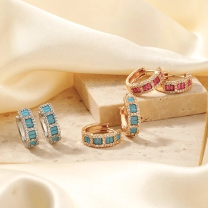 Exquisite Creolen mit bunten Edelsteinen und Diamanten auf Marmor und Seidenstoff