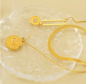 Detail of gold double layer snake chain necklace with coin pendant on glass surface