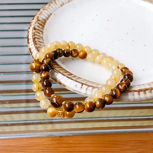 Close-up of white crystal and tiger eye beaded bracelets with a gold coin charm in a ceramic dish