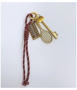 Detail of red braided cord keychain with gold tennis racket, abacus, and key charms