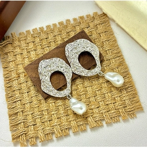 Detail of silver hammered hollow earrings with white baroque pearls on a rustic wood base