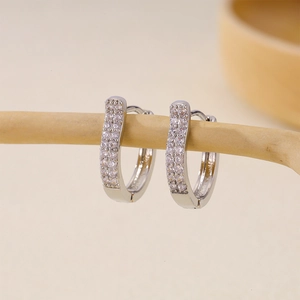 Close-up of silver U-shaped earrings set with rows of sparkling zircon on wooden branch