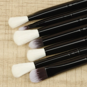 Detail of 7-piece eye makeup brush set with black handles on beige fabric texture