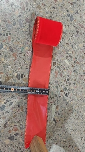 Detail view of red velvet ribbon with gold edges being measured at 6.3cm width