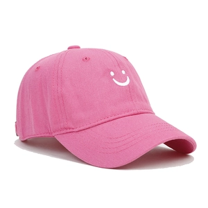 Detail of pink cotton baseball cap featuring a white embroidered smile face and stitching