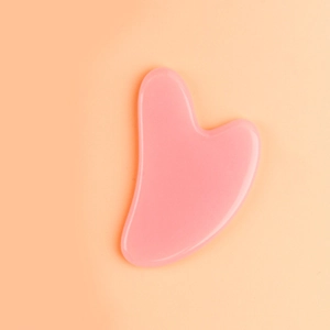 Detailed view of a heart-shaped pink resin facial massage tool on an orange background